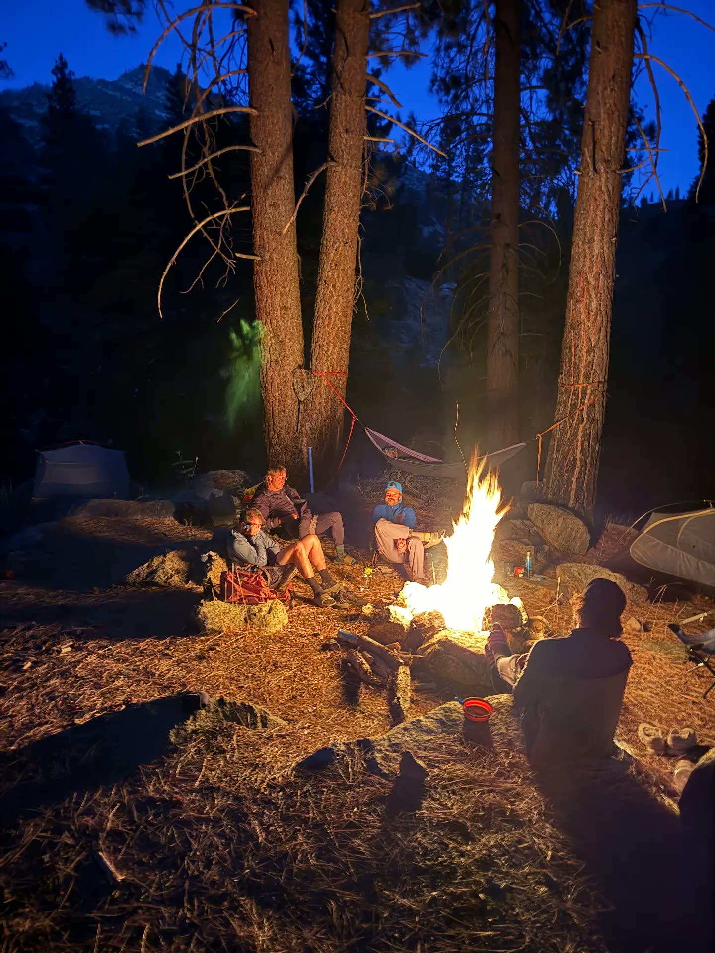 The group around the campfire at dusk with tents and a hammock in camp during outdoor therapy