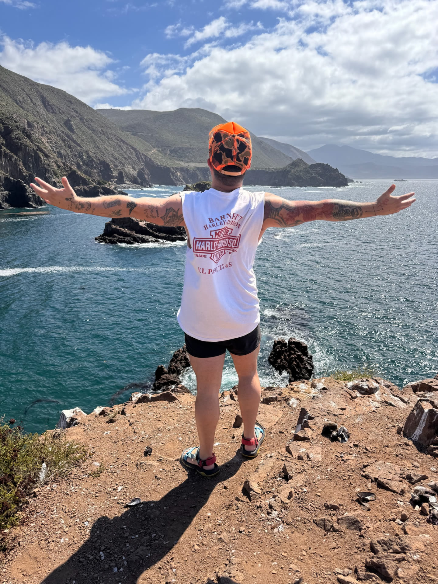 Man standing arms-wide on a cliff above the Baja coastline during a wilderness therapy trip
