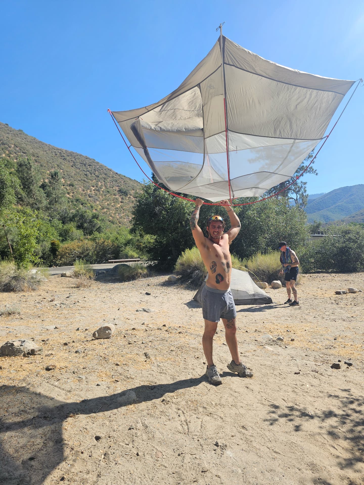 Man hoisting a tent overhead at camp during a men's camping trip in Sequoia National Forest