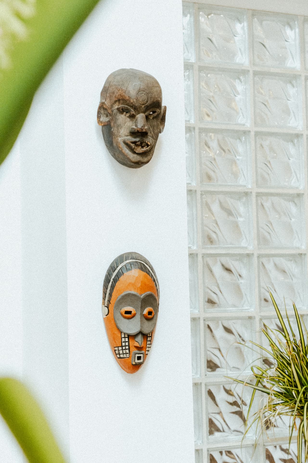 Carved masks on a white wall beside glass block at Recovery Republic