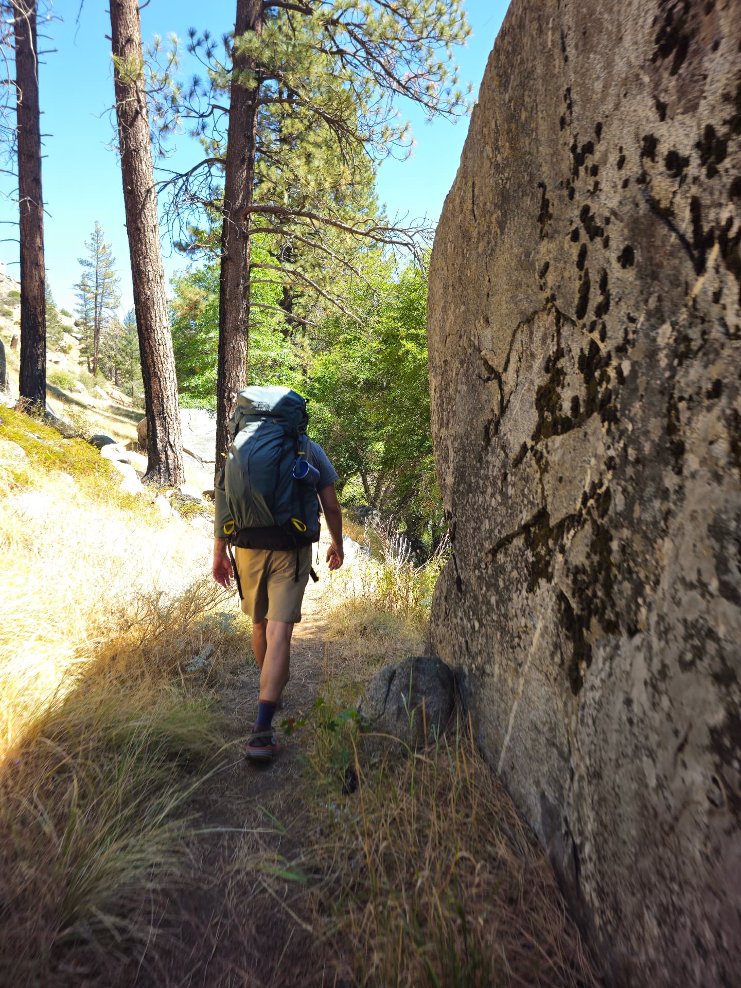 Backpacker walking a narrow trail past a granite boulder in Sequoia National Forest